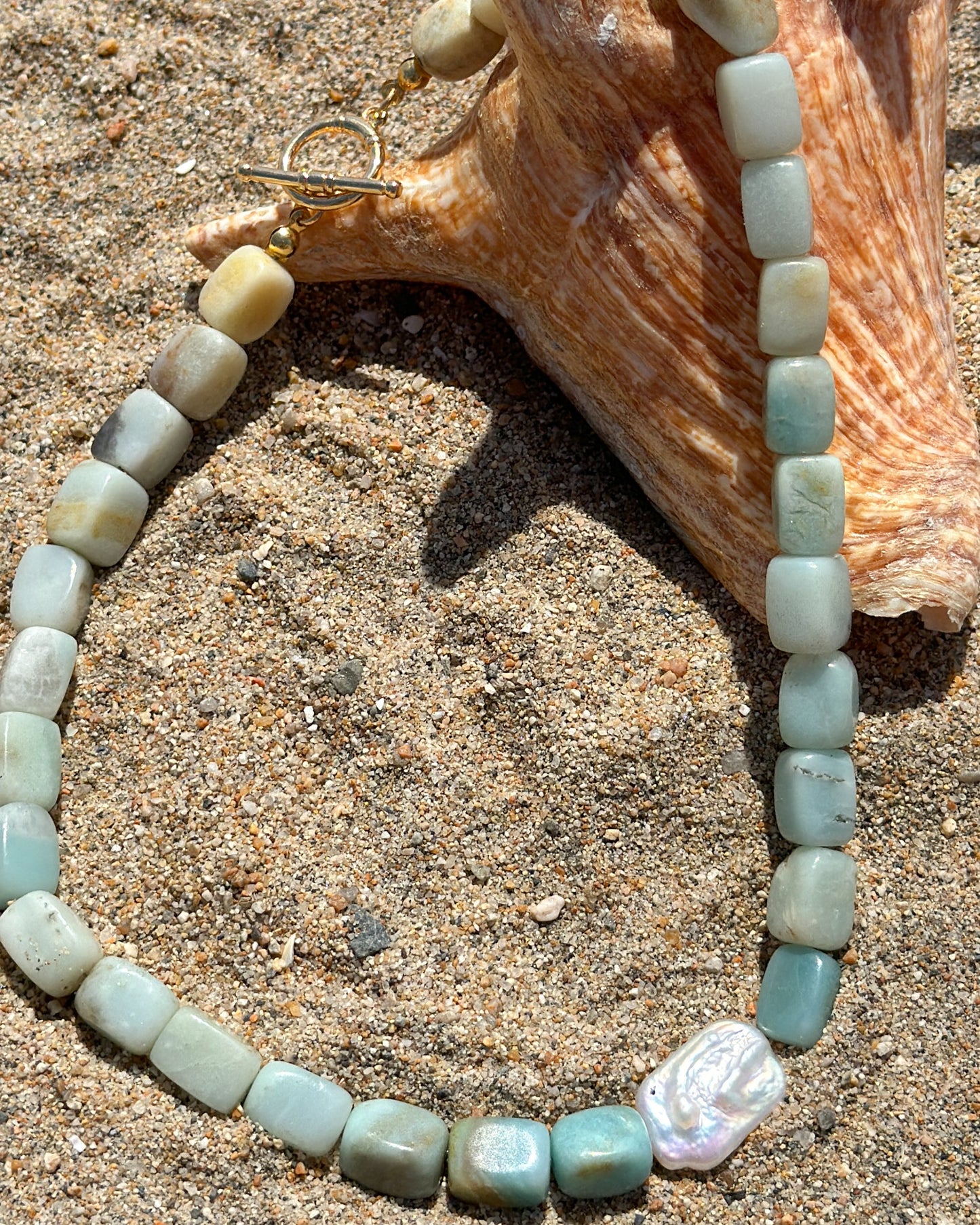 Beaded necklace on sand with a shell in the background