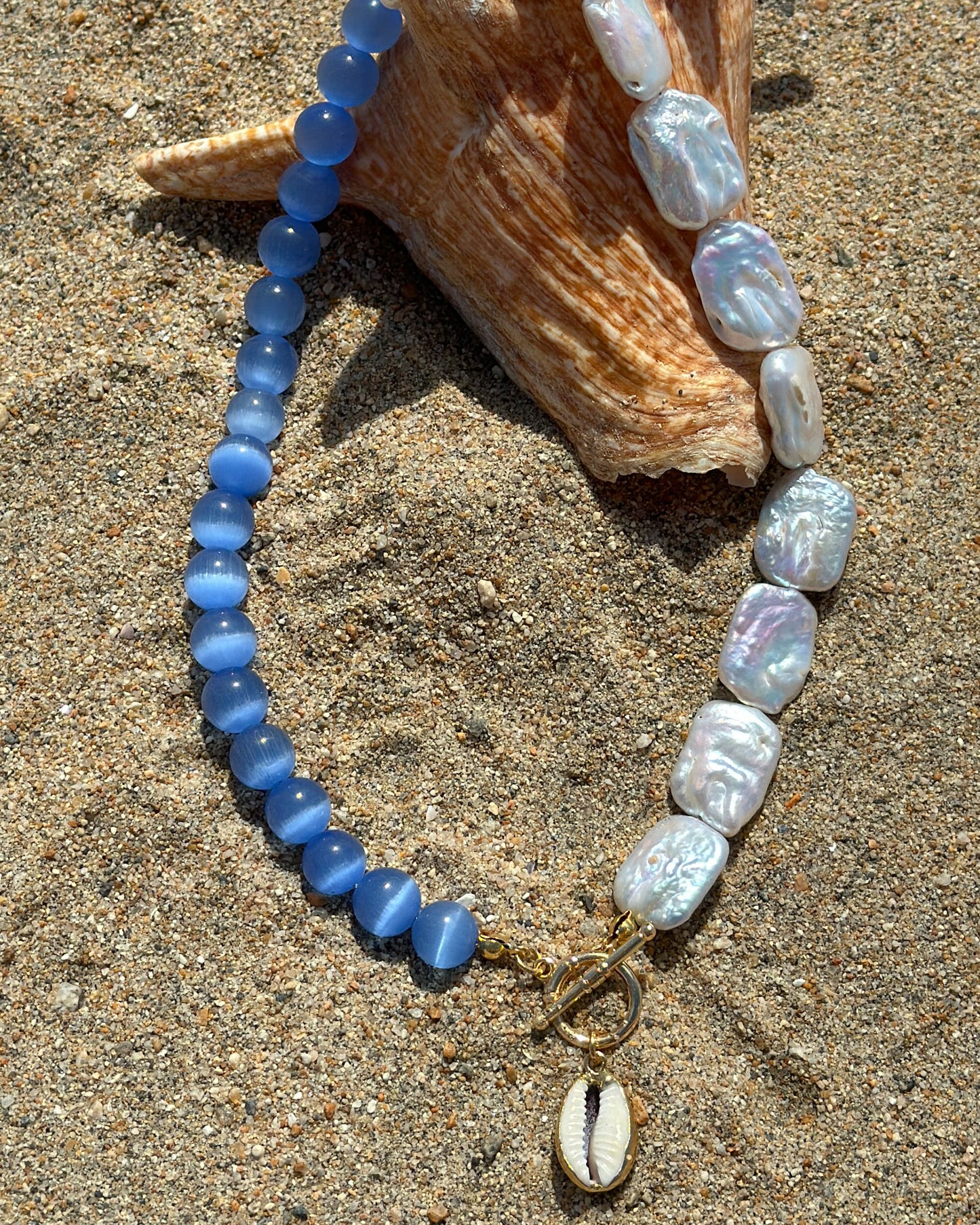 Necklace with blue and white beads on a shell on sand