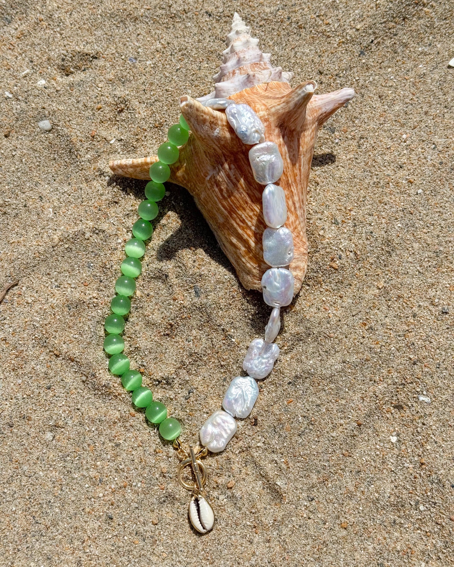 Necklace with green and white beads on a shell on sandy surface