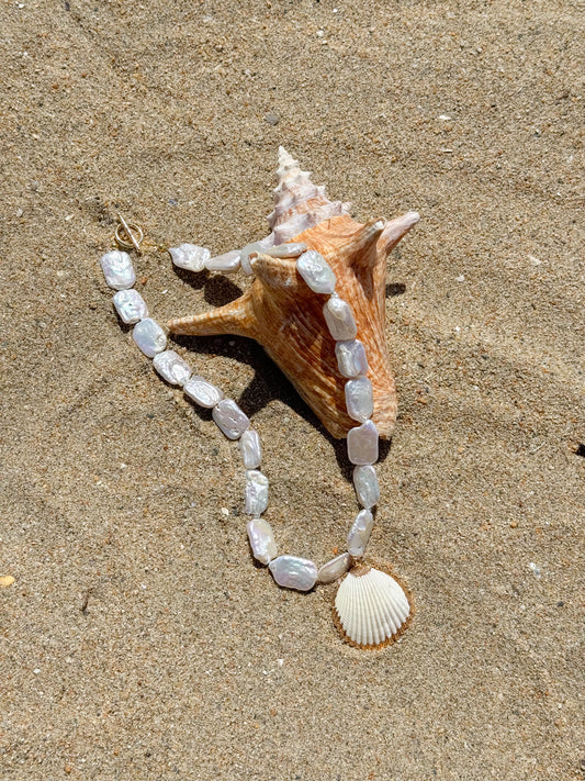 Pearl and shell necklace with a large conch shell on sand