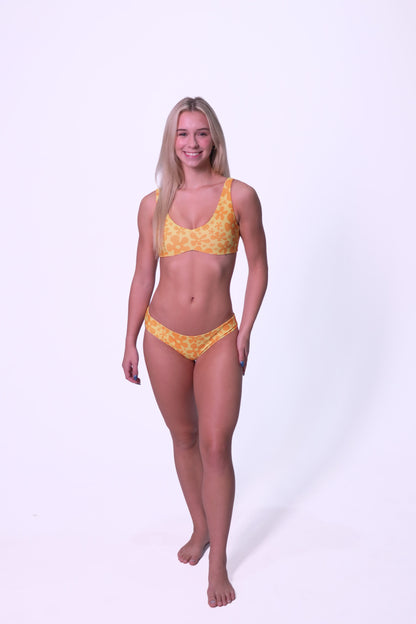 women modeling orange and yellow floral bikini against a plain light backdrop. 