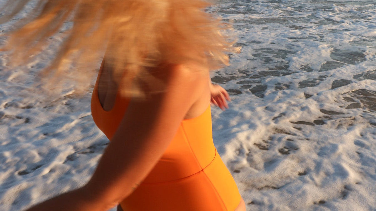 girl wearing orange one piece swimsuit while playing in the ocean