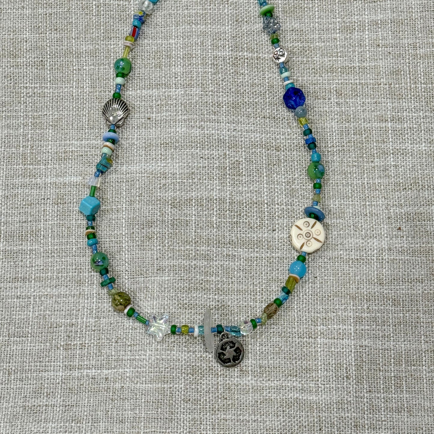 Handmade beaded necklaces with sea glass found on the shores of Lake Michigan. Contains recycle sign charm