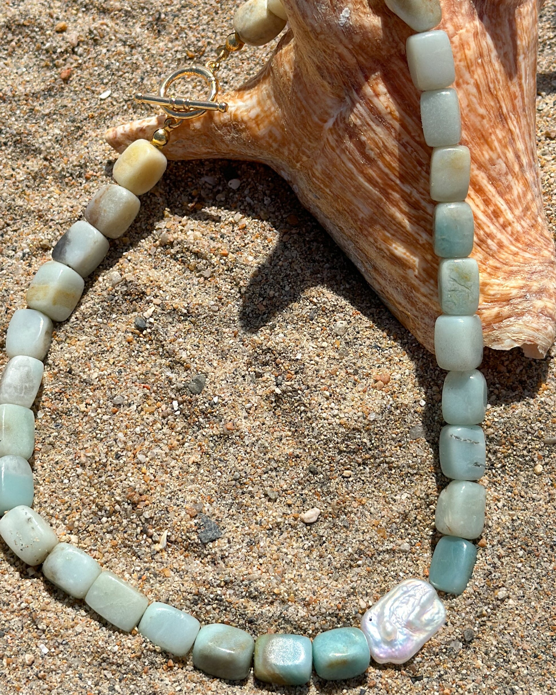 Beaded necklace on sand with a shell in the background