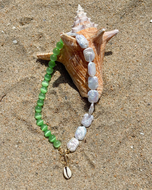 Necklace with green and white beads on a shell on sandy surface