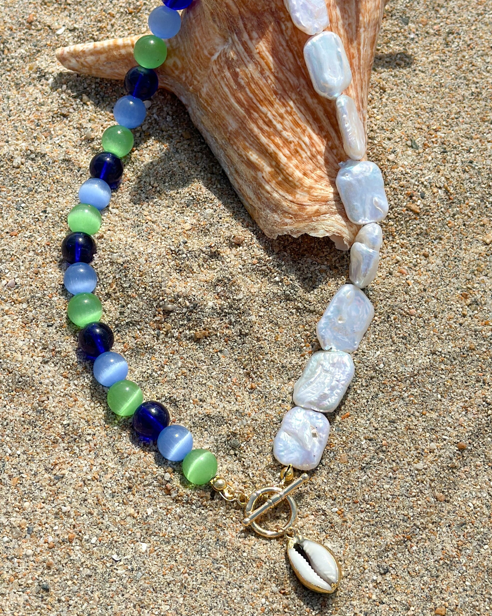 Necklace bracelet with blue, green, and white stones on a sandy background