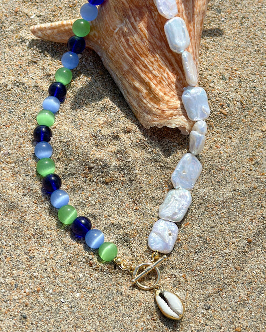 Necklace bracelet with blue, green, and white stones on a sandy background